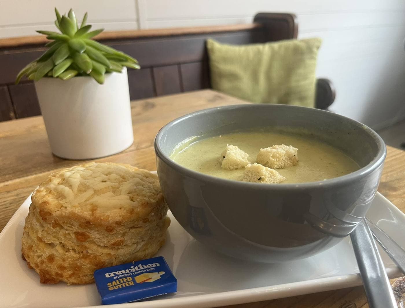 Cheese scone beside a bowl of broccoli soup with croutons, Trewithen salted Cornish butter on a wooden table