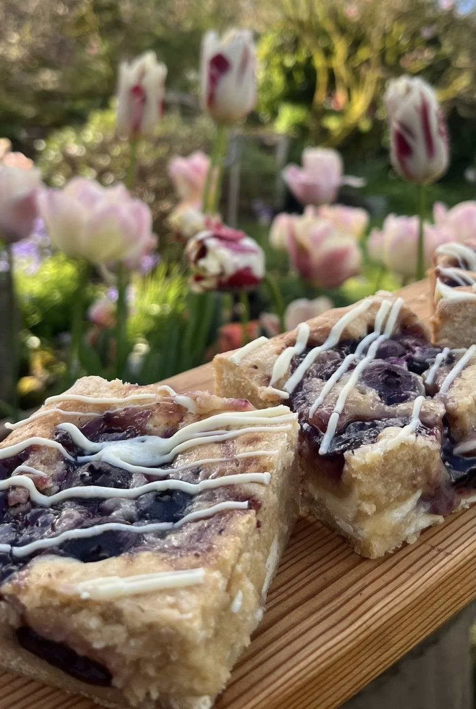 Homemade blueberry blondies drizzled with white chocolate, styled with pink and red tulips